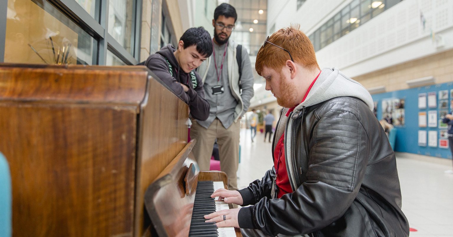 Keighley College student playing the piano at Keighley College with other students watching