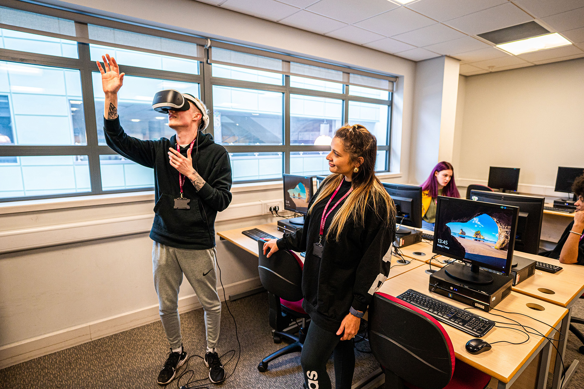 A female student looking at a male student experiencing on the Virtual Reality in the classroom