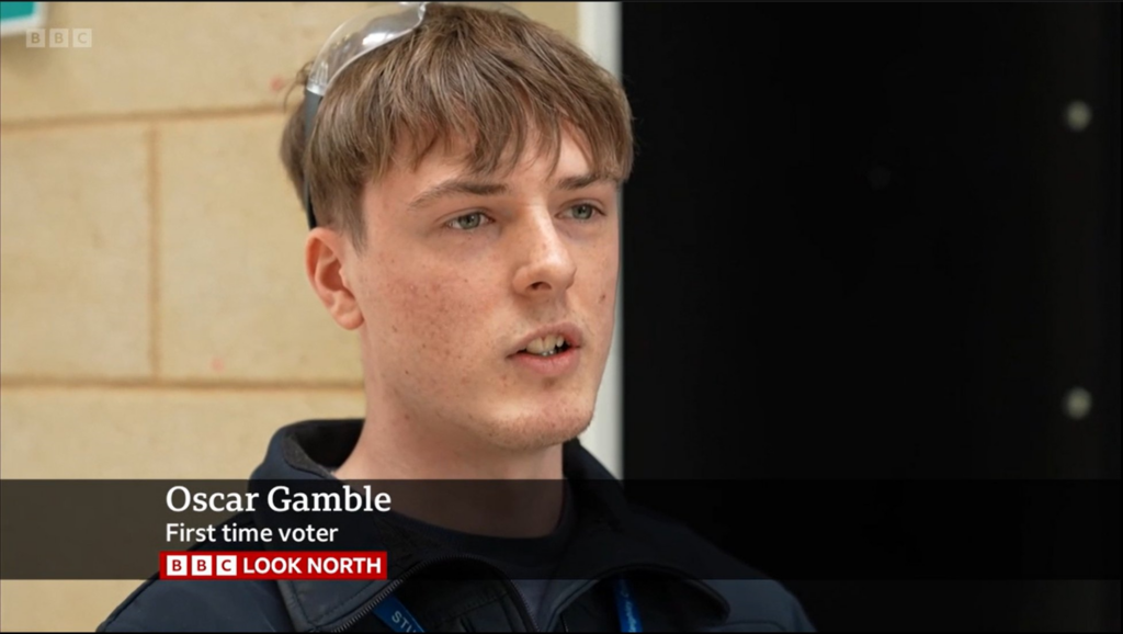 A teenage boy wearing a dark shirt is appears on a television screen showing the evening news. He is speaking mid-sentence to the camera.