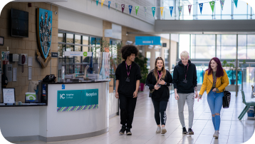 Four students smiling and walking through the main Keighley College foyer past the reception desk
