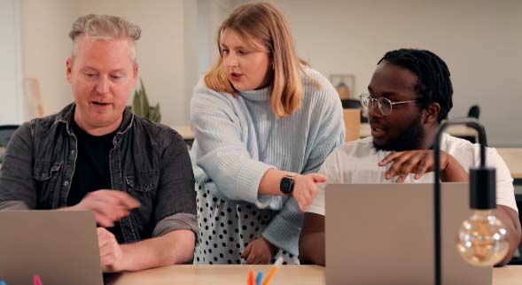 Three people in discussion, chatting whilst all looking at two laptop screens