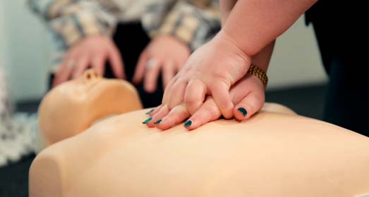 Hands performing CPR on a medical mannequin during First Aid training