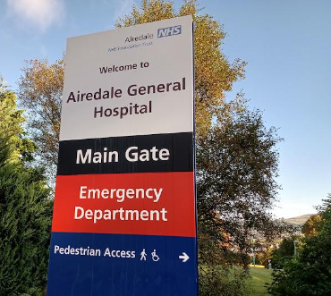 A tall sign with text that says 'Welcome to Airedale General Hospital', followed by directions to the main gate, emergency department and pedestrian access.