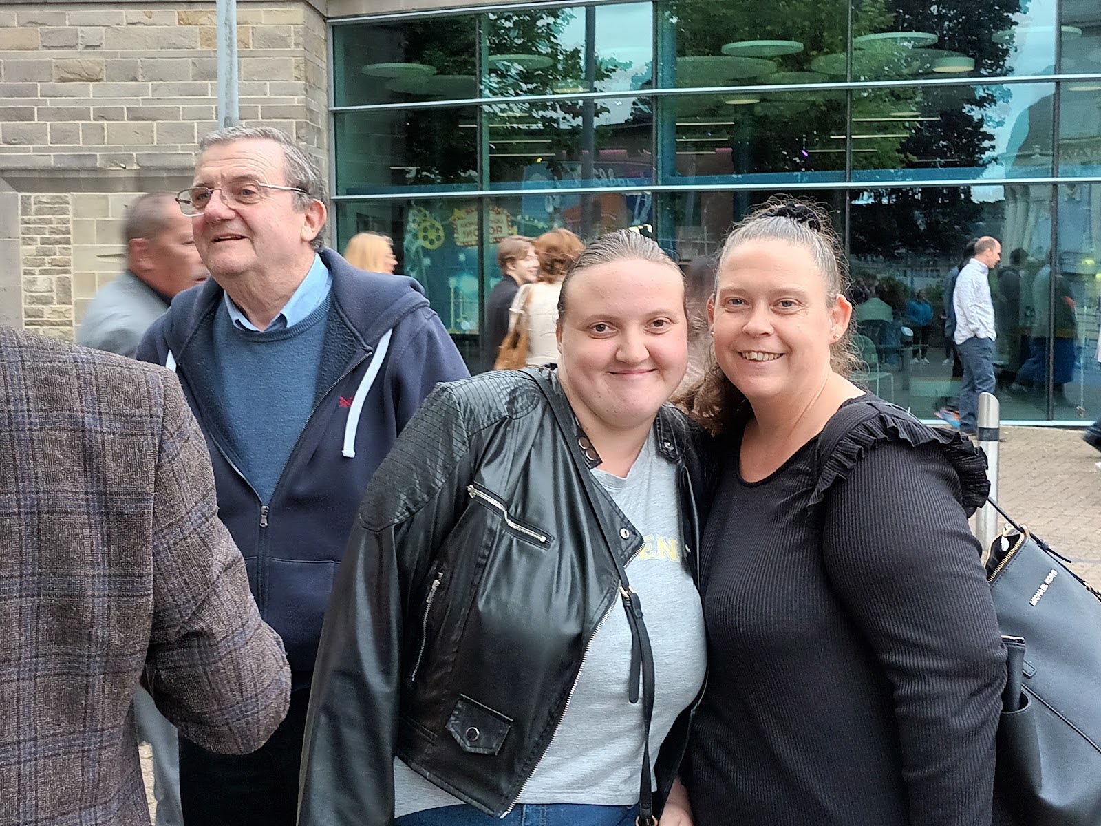 A group of people are milling around outside a building. Two women smile for the camera