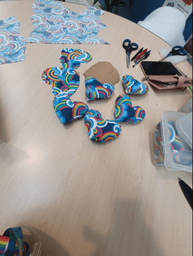 A round table displaying a collection of colourful fabric hearts with scissors and pens scattered nearby