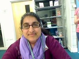 A woman wearing glasses and a purple scarf sits at a table looking focused