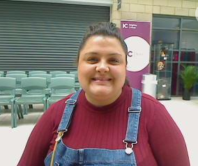 A woman wearing a red top smiles to the camera whilst standing in an auditorium