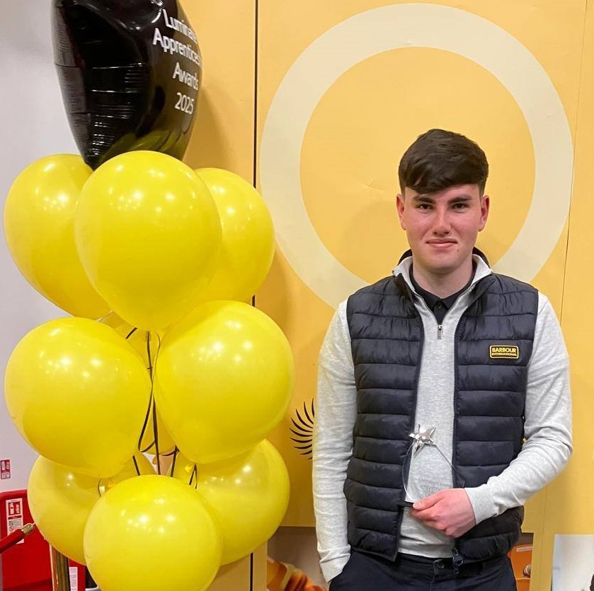 Keighley College apprentice Sam Holder standing beside yellow balloons at an awards ceremony
