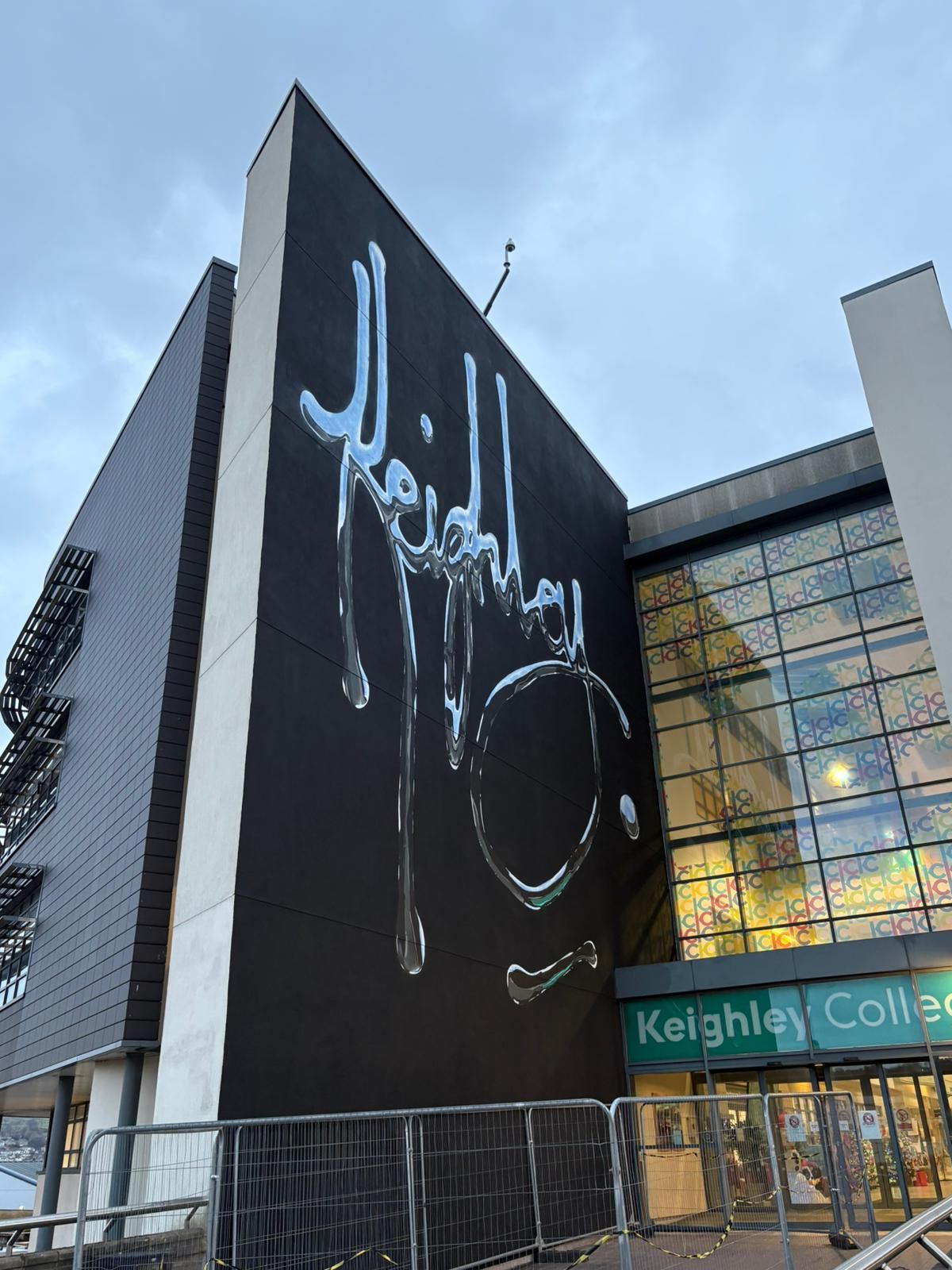 Image of Keighley College entrance with large street art mural on left side of the entrance. The wall is painted black and the word 'Keighley' has been painted on top in silver, reflective, liquid style font.