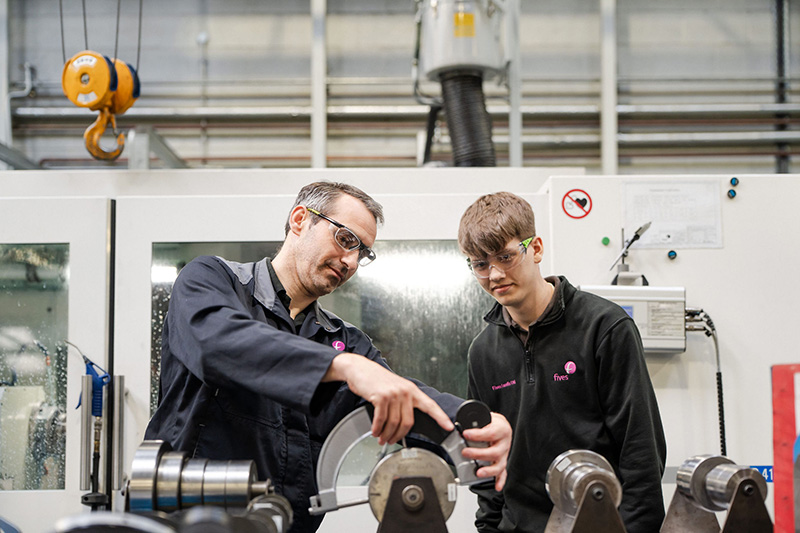Engineering apprentice learning how to work machinery with teacher