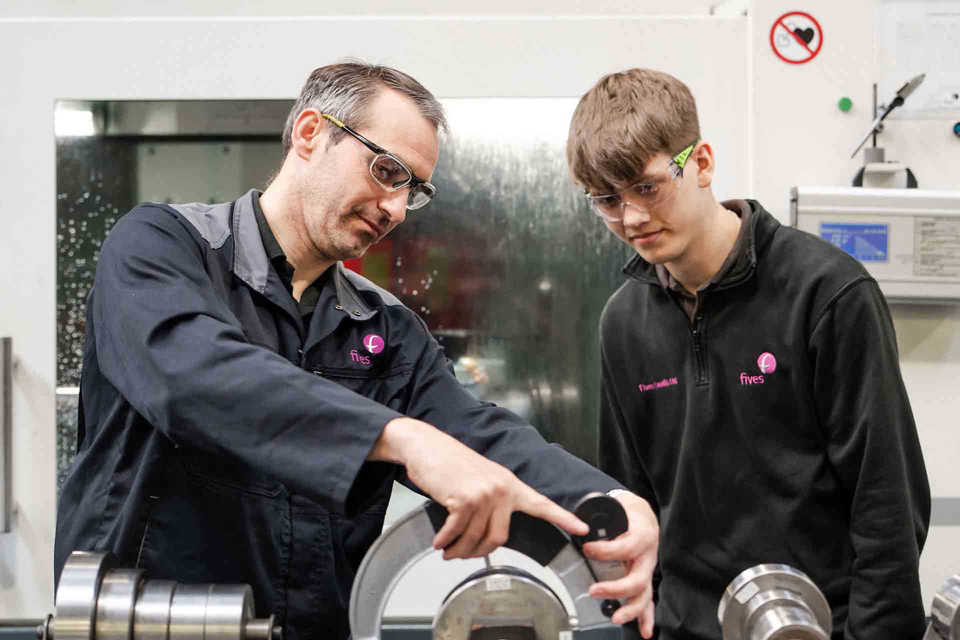 Engineering apprentice learning how to work machinery with teacher