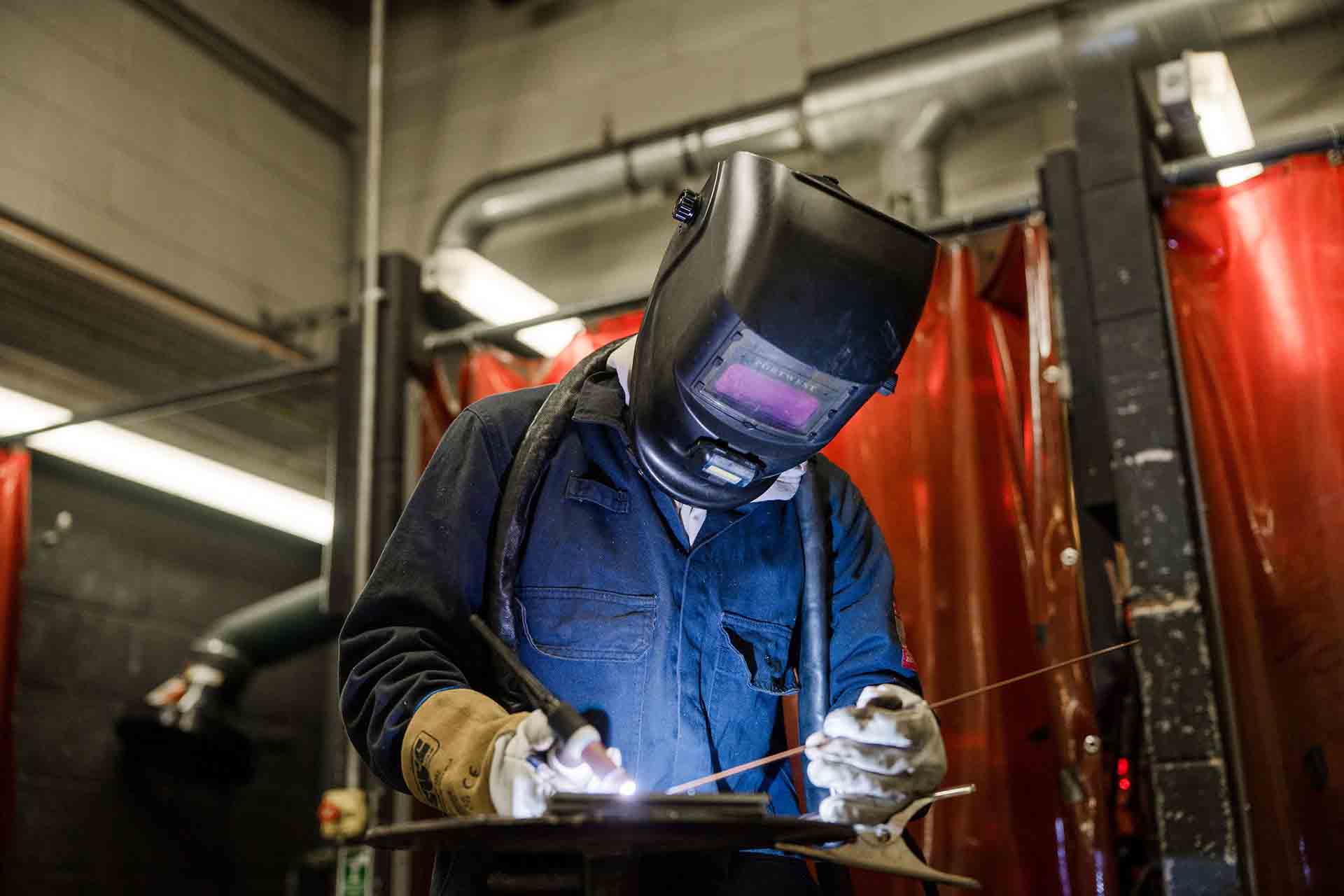 A construction student wearing uniform and safety goggles welding fabrication
